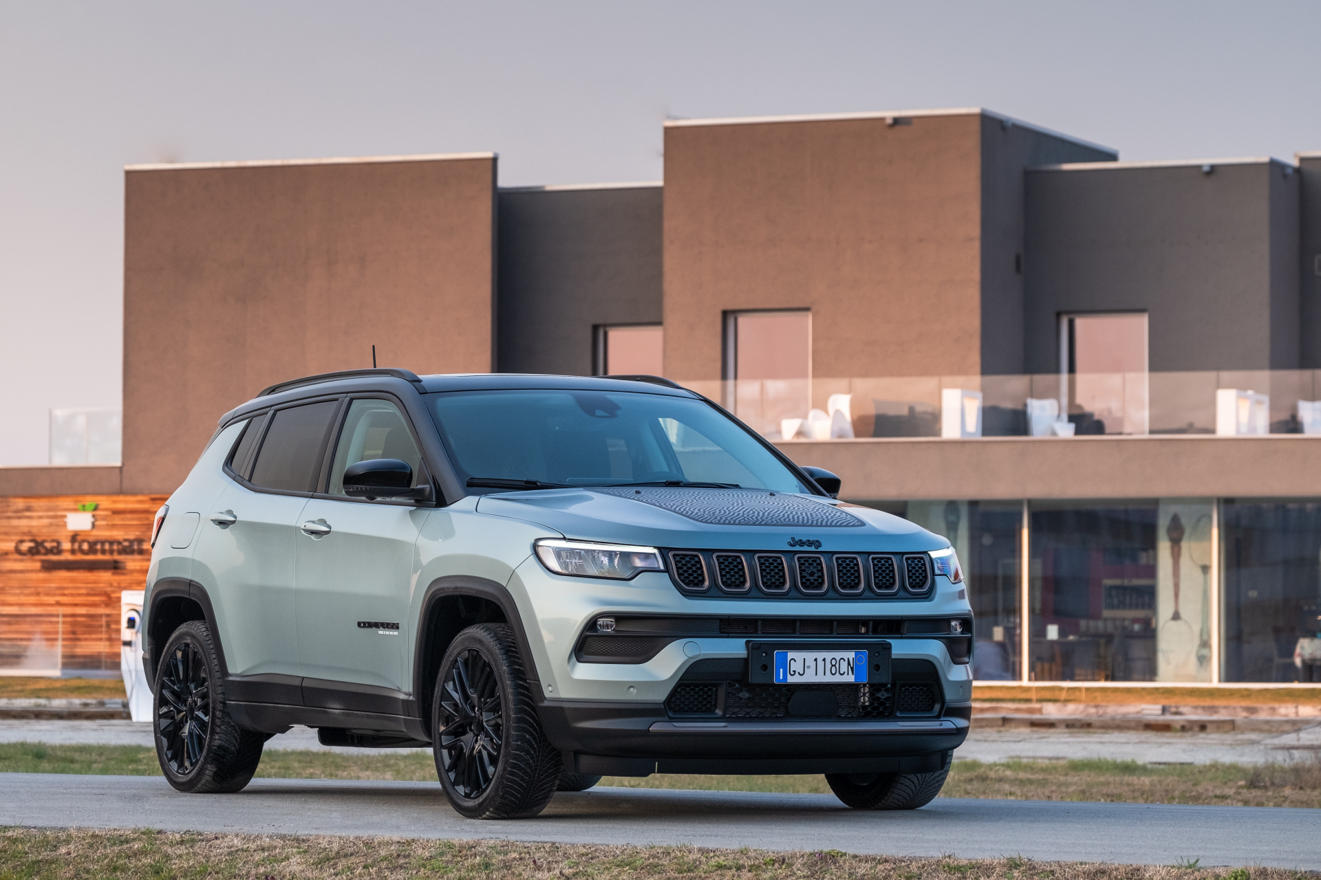 Jeep Compass 4xe Upland de couleur gris pâle stationnée devant un bâtiment moderne.