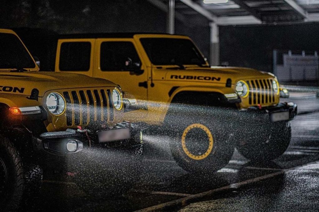 Deux SUVs Jeep Rubicon jaunes illuminent la nuit sous une pluie battante, mettant en avant leur robustesse et leur performance dans des conditions météorologiques difficiles.