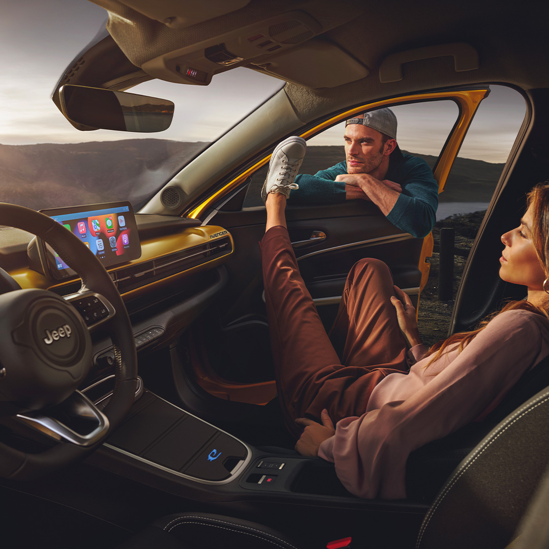 Un homme et une femme profitant de l'intérieur confortable et connecté d'un SUV Jeep Avenger jaune, avec une vue sur les montagnes en arrière-plan