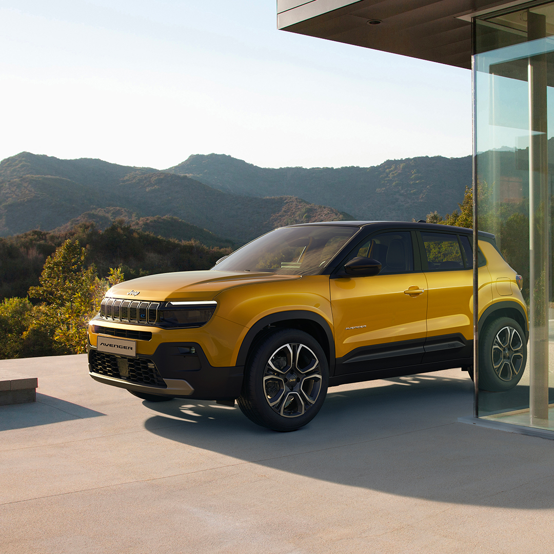 Jeep Avenger jaune garée devant une maison moderne avec des montagnes en arrière-plan